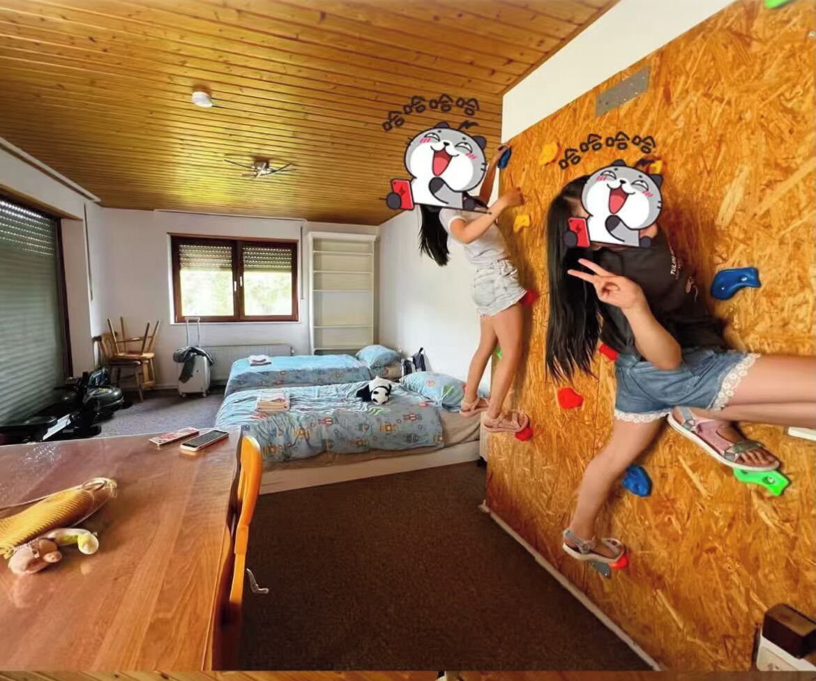 A room with a climbing wall, a bed, a desk, and a window.