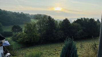 Ländliche Landschaft mit einem Gebäude, an dem die Zahl '14' angebracht ist, umgeben von Bäumen und Feldern.
