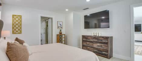 Une chambre à coucher comprenant un lit, une commode, un téléviseur et une porte donnant sur un balcon.