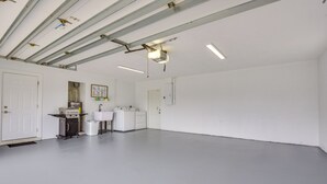 Een schone, lege kamer met witte wanden en een grijze vloer, met een kitchenette inclusief een kookplaat, spoelbak en opbergkasten.