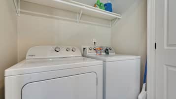 Un área de lavandería con lavadora y secadora Whirlpool, un estante con productos de limpieza y una puerta a la derecha.