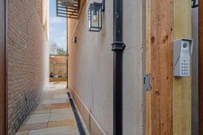 A narrow corridor with a brick wall on one side and a wooden door on the other, a tiled floor, and a security keypad. - Fulham Pet Friendly Studio, Sleeps 2 With Patio (London)