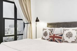 A bed with white bedding, a lamp, and a view through a window with curtains. - Fulham Pet Friendly Studio, Sleeps 2 With Patio (London)