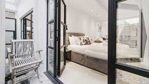 A bedroom with a bed, a bench, and a glass door leading to a balcony. - Pet Friendly Studio in Fulham, Sleeps 2 (London)