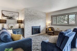 Ein modernes Wohnzimmer mit Kamin aus Stein, blauen Sofas und einem großen Fenster.
