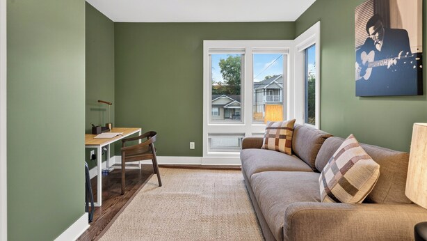 A living room with a sofa, a table, and a chair. There is a window with a view of houses outside. - Hot Tub + Rooftop Lounge + Game Room | Buchanan Arts | The Mod Buchanan (Nashville)
