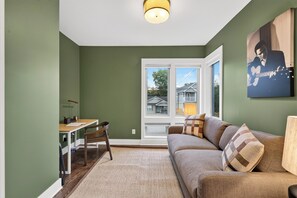 Un salón con un sofá, una mesa y una silla. Se ve una ventana con vistas a casas.