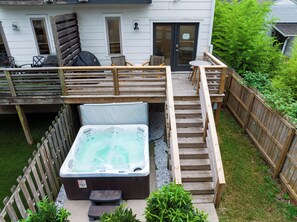 A hot tub on a wooden deck with steps leading to a house. - Hot Tub + Rooftop Lounge + Game Room | Buchanan Arts | The Mod Buchanan (Nashville)