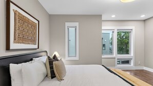 A bedroom with a large bed, a framed artwork, a window, and a view of the outside. - Hot Tub + Rooftop Lounge + Game Room | Buchanan Arts | The Mod Buchanan (Nashville)