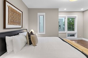 Ein Schlafzimmer mit einem großen Bett, einem gerahmten Kunstwerk, einem Fenster und Blick ins Freie.