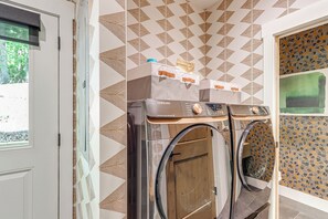 A laundry room with two Samsung washing machines, patterned walls, and a door with a view of greenery outside. - Screened Porch + Home Office: Modern Ellijay Cabin (Ellijay)