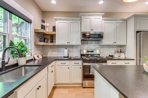 A modern kitchen with white cabinets, stainless steel appliances, and a large window. - Screened Porch + Home Office: Modern Ellijay Cabin (Ellijay)