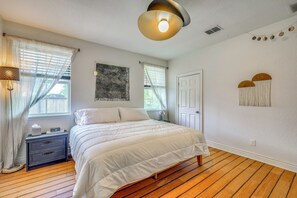 Ein Schlafzimmer mit einem Bett, einem Nachttisch, einer Lampe, einem Fenster mit Vorhängen und einer Wandleuchte.