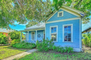 A two-story house with a porch, surrounded by greenery. - Walk to the Alamodome! Quirky Gem w/ Private Patio (San Antonio)
