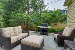 Un patio al aire libre con mobiliario de mimbre, una parrilla y una cerca de madera.