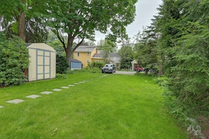 A residential property with a paved driveway leading to a parked car, surrounded by lush greenery and a small shed. - 'The Hand House!' Walk to Downtown & Race Course (Saratoga Springs)