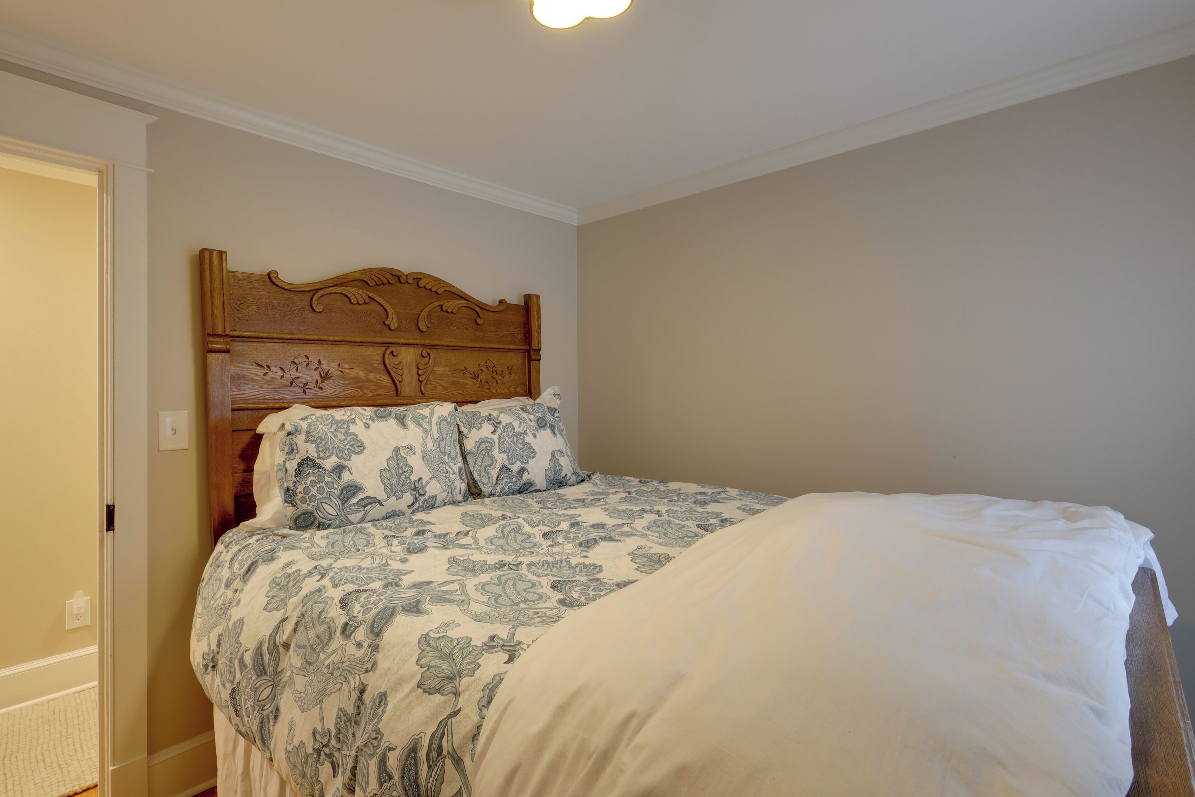 A bedroom with a wooden headboard, a floral-patterned bedspread, and a white comforter.