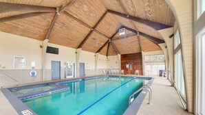 Ein Hallenbad mit Holzbalkendecke, einem Rettungsschwimmerstuhl und einem Poolbereich mit Liegestühlen.