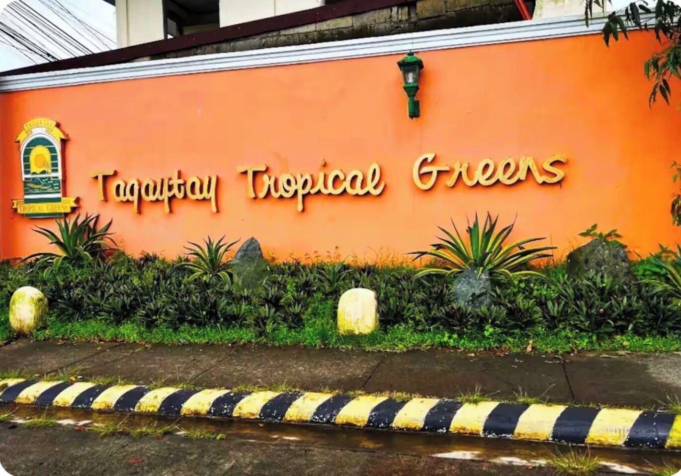 A sign for 'Tagaytay Tropical Greens' with tropical plants and a lamp post.