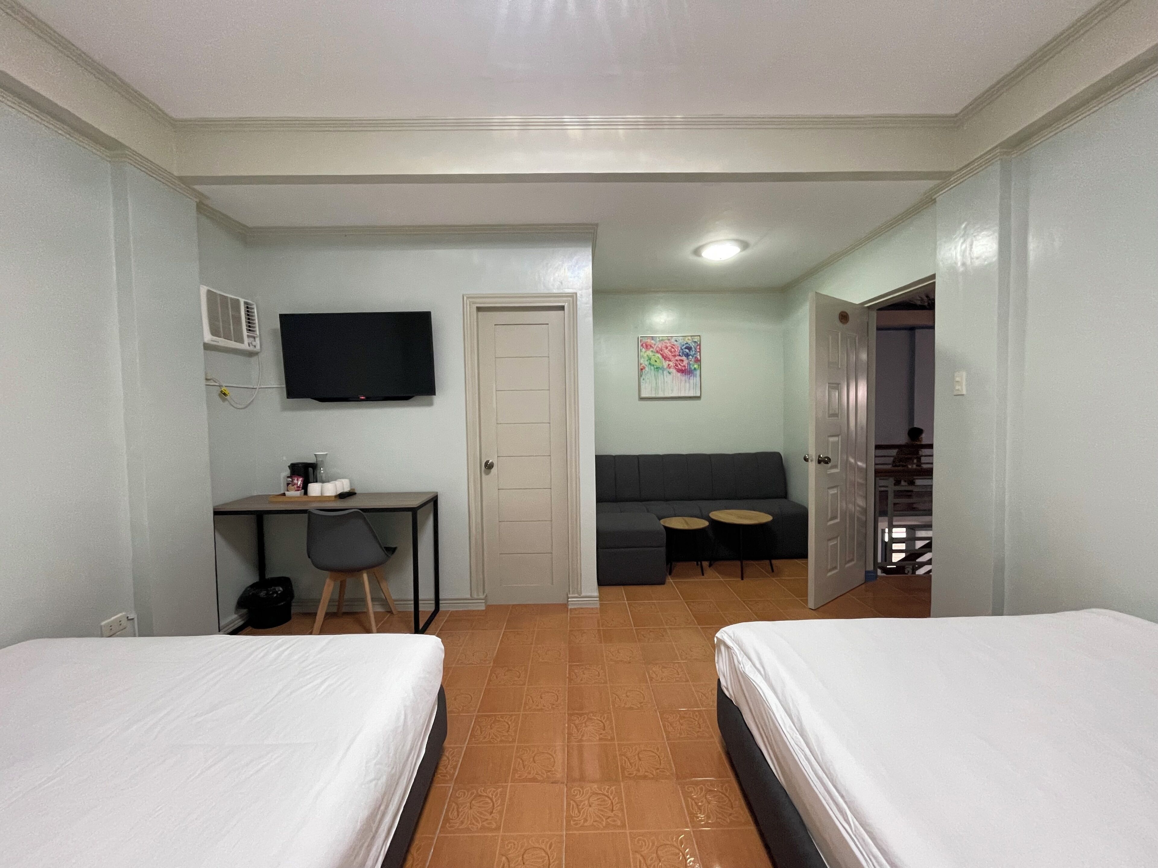 A hotel room with two beds, a desk with a chair, a television, a sofa, and a small table.