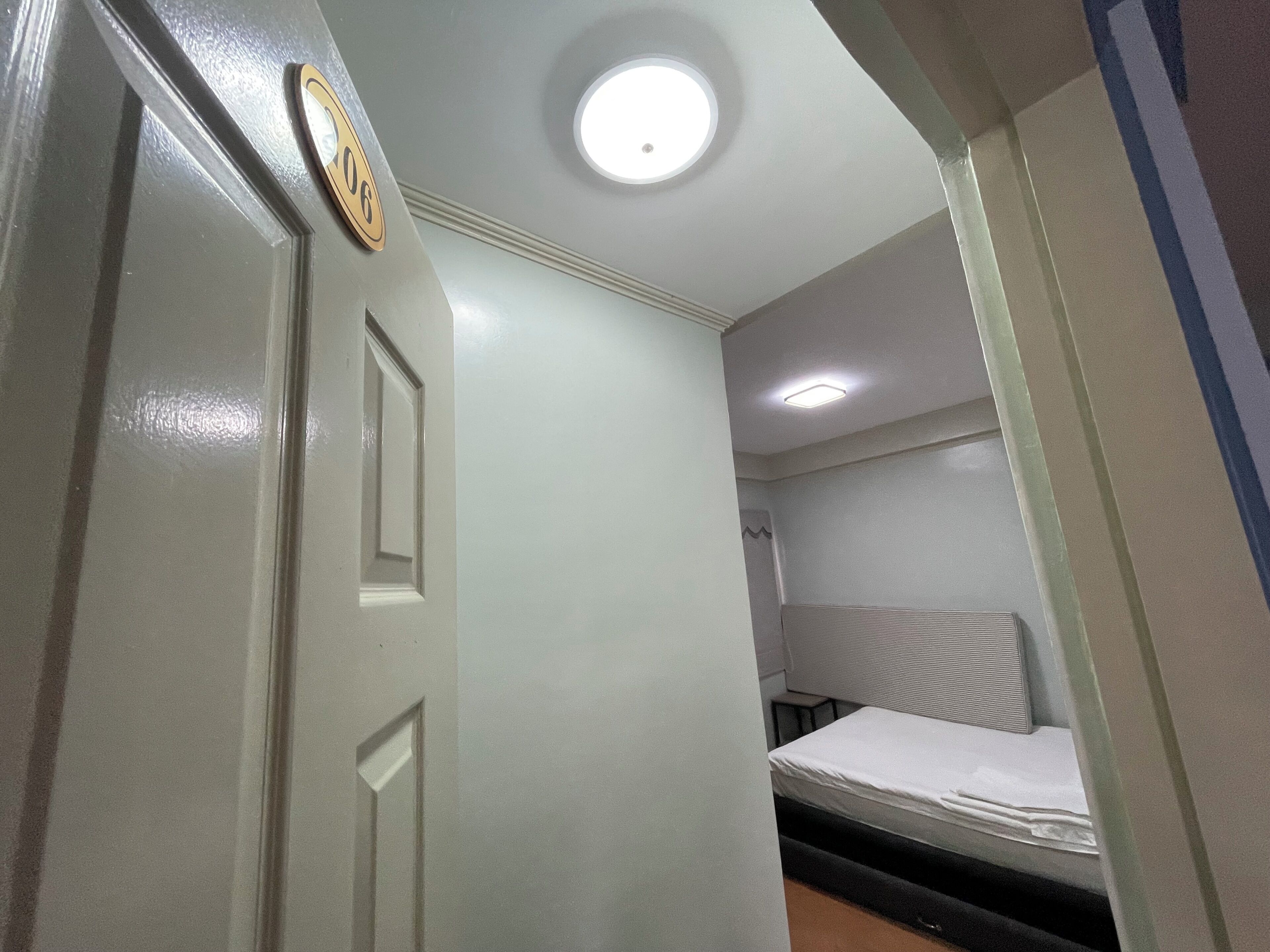 A room with a bed, a door with a number, and a ceiling light.