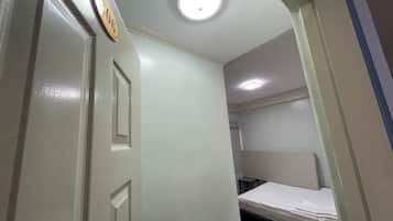 A room with a bed, a door with a number, and a ceiling light.