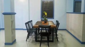 A dining area with a rectangular table surrounded by chairs, a potted plant on the table, and a window above. - Serene 7-Bedroom Retreat House near Attractions and Dining Tagayay (Tagaytay City)