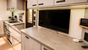 A modern kitchen with built-in appliances, a large flat-screen TV, and a minimalist design. - Modern Houseboat 'Tegel' with Lake View, Wi-Fi & Air Conditioning (Berlin)