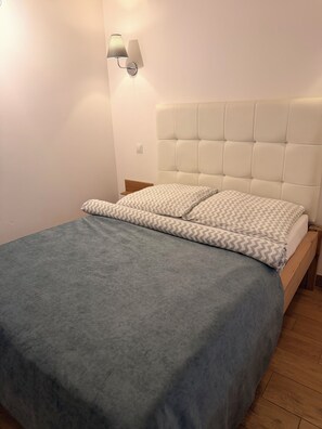 Un dormitorio con cama, cabecera, mesita de noche y lámpara de pared.