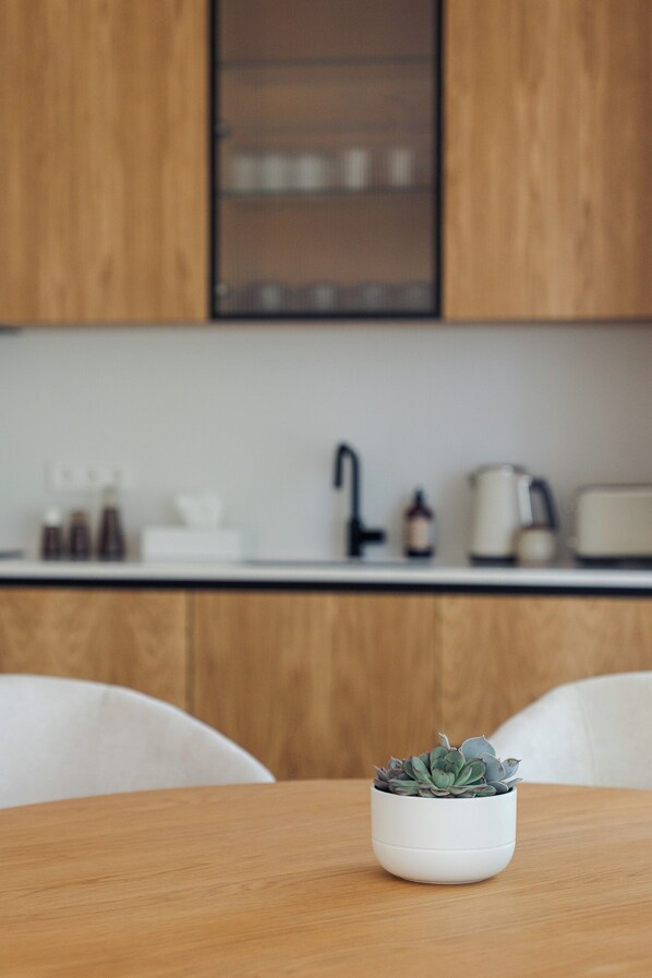 A modern kitchen with wooden cabinets, a white countertop, and a small potted plant on a wooden table.