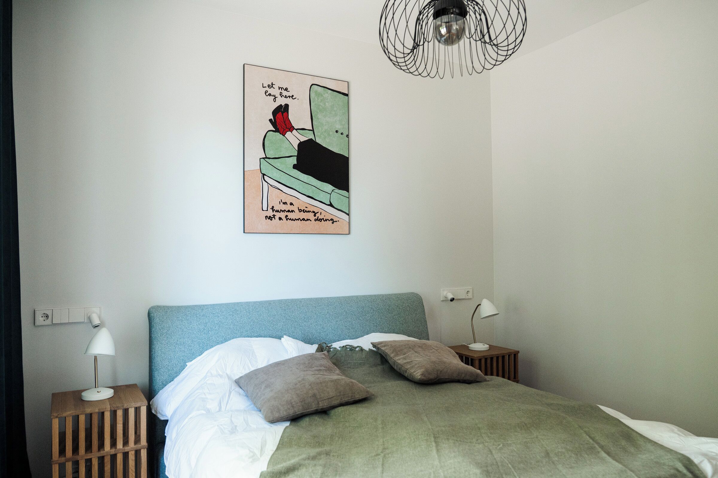 Un dormitorio con una cama, dos mesitas de noche, una lámpara de pared, una obra de arte en la pared y un aplique de techo.