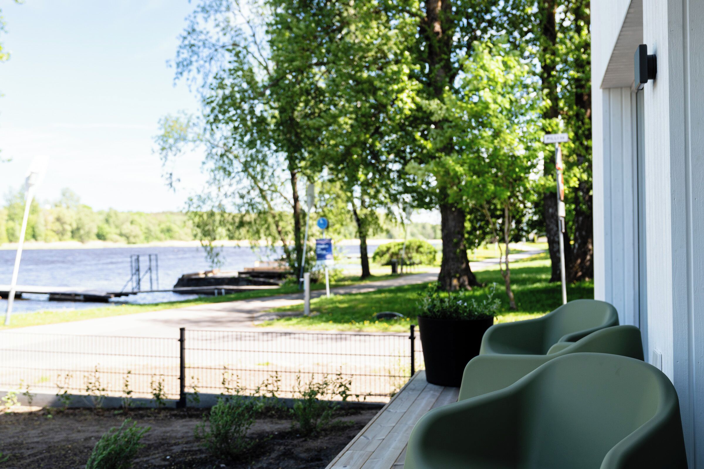 A view of a lakeside property with a wooden deck, a row of green chairs, and a white building.