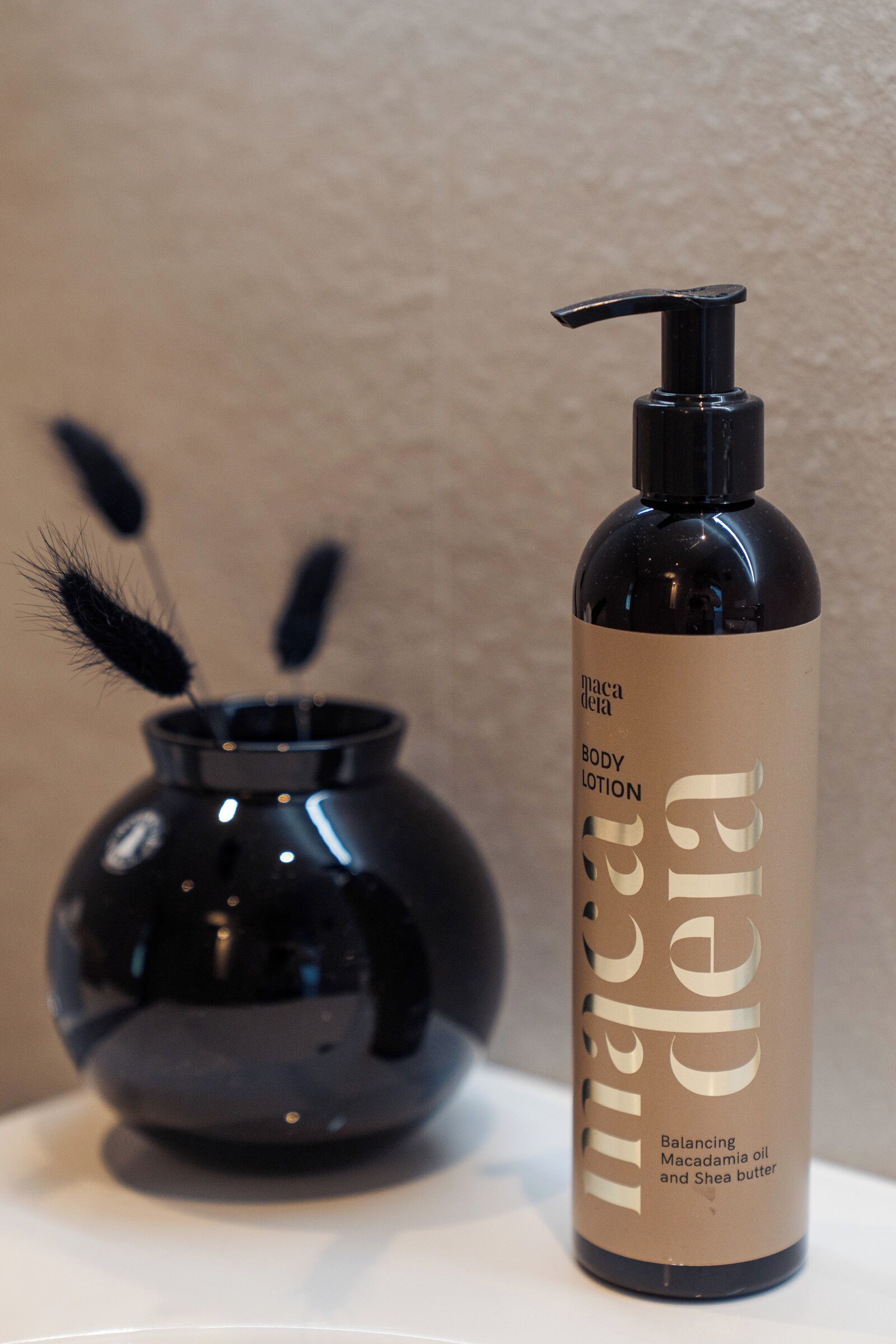 A body lotion bottle labeled 'maca de la' next to a black vase with decorative elements.