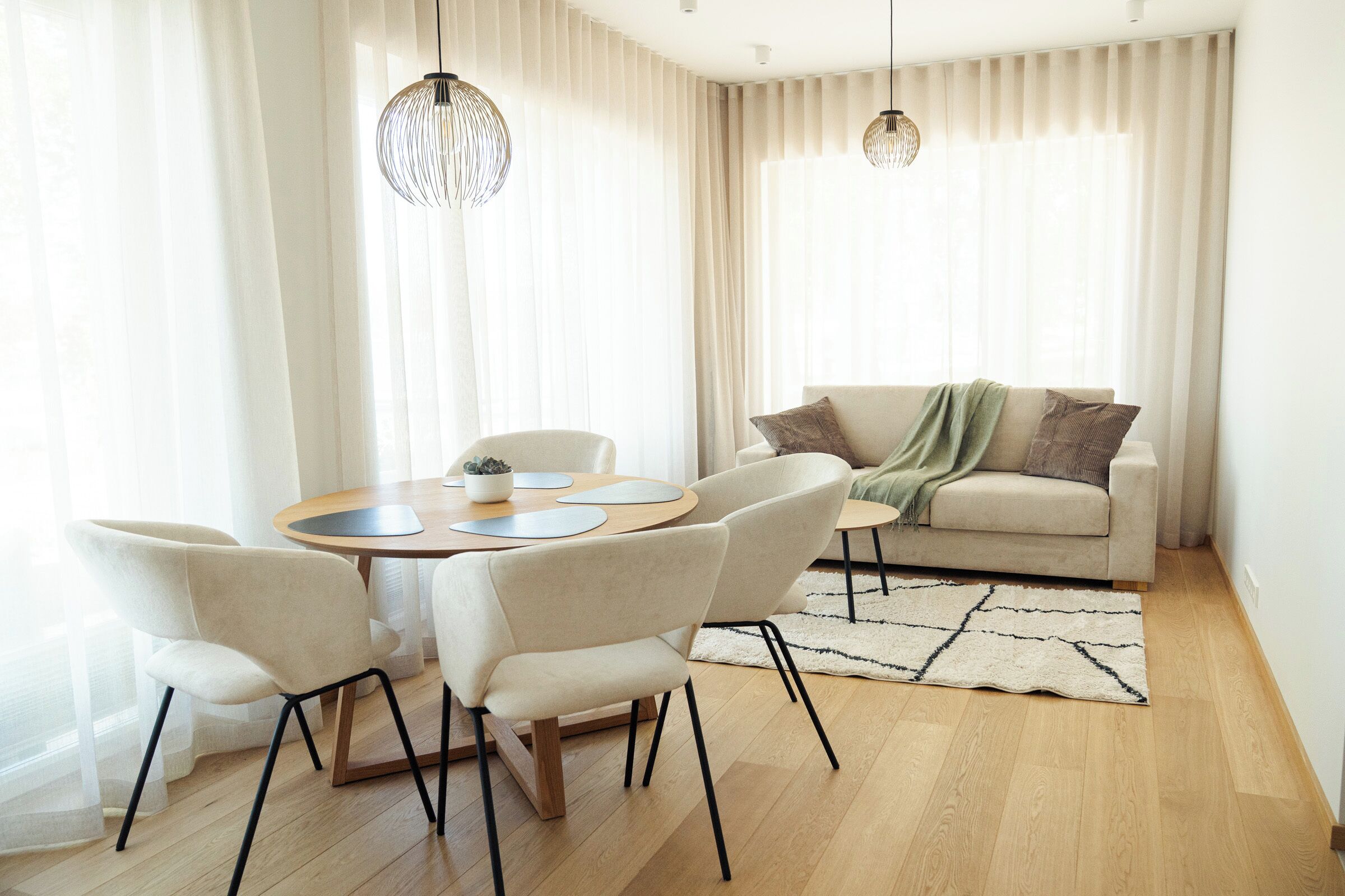 Un salon moderne avec une table ronde en bois, quatre chaises, un canapé et deux lampes suspendues.