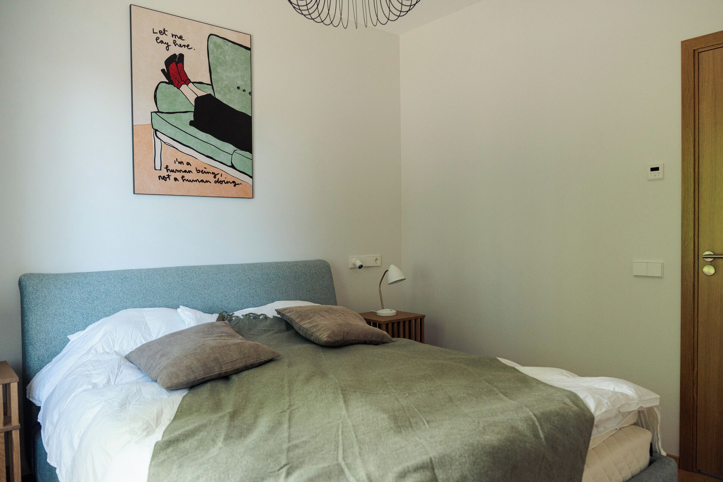 A bedroom with a bed, pillows, a bedside table with a lamp, a wall clock, and a door.