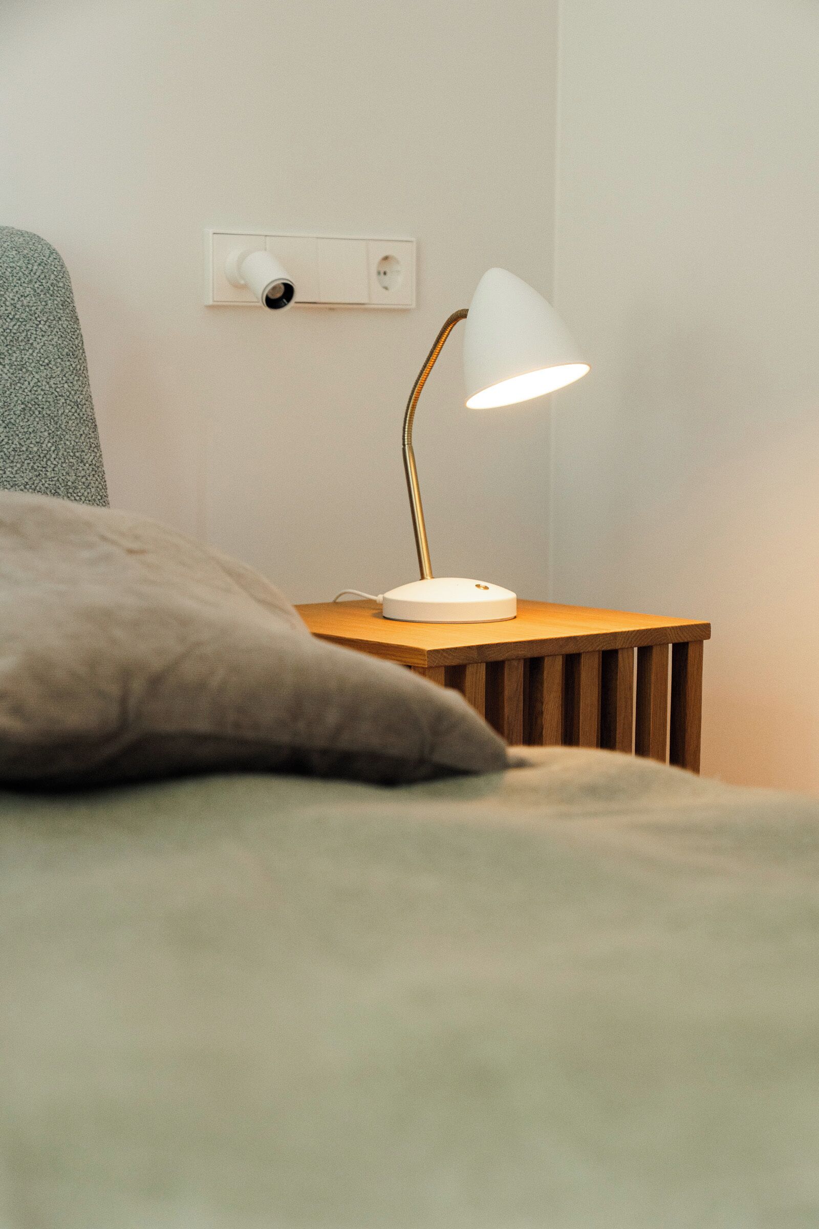 En seng med pude, et natbord med lampe og en stikkontakt.