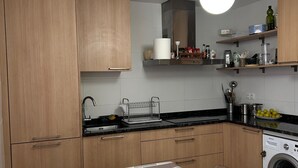 A compact kitchen with wooden cabinets, a built-in washing machine, and a dining area with a patterned tablecloth.