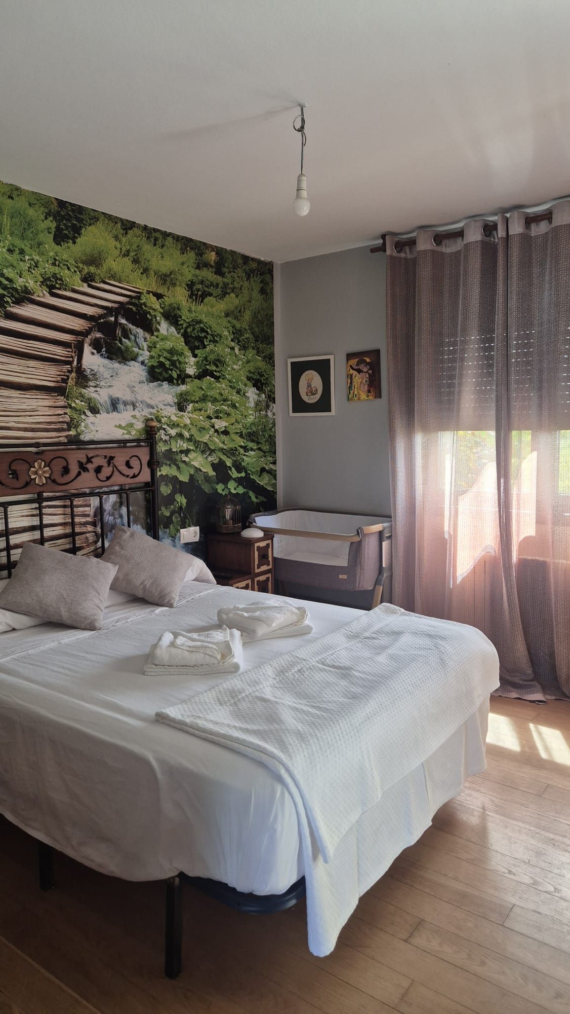 Un dormitorio con una cama, un mural en la pared, una cuna y una ventana con cortinas.