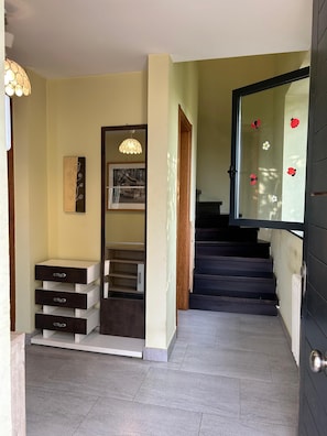 A hallway with a staircase, a wooden cabinet with drawers, a hanging light fixture, and a door with a glass panel. - As Pintiñas da Xoaniña Country House (Santiago de Compostela)