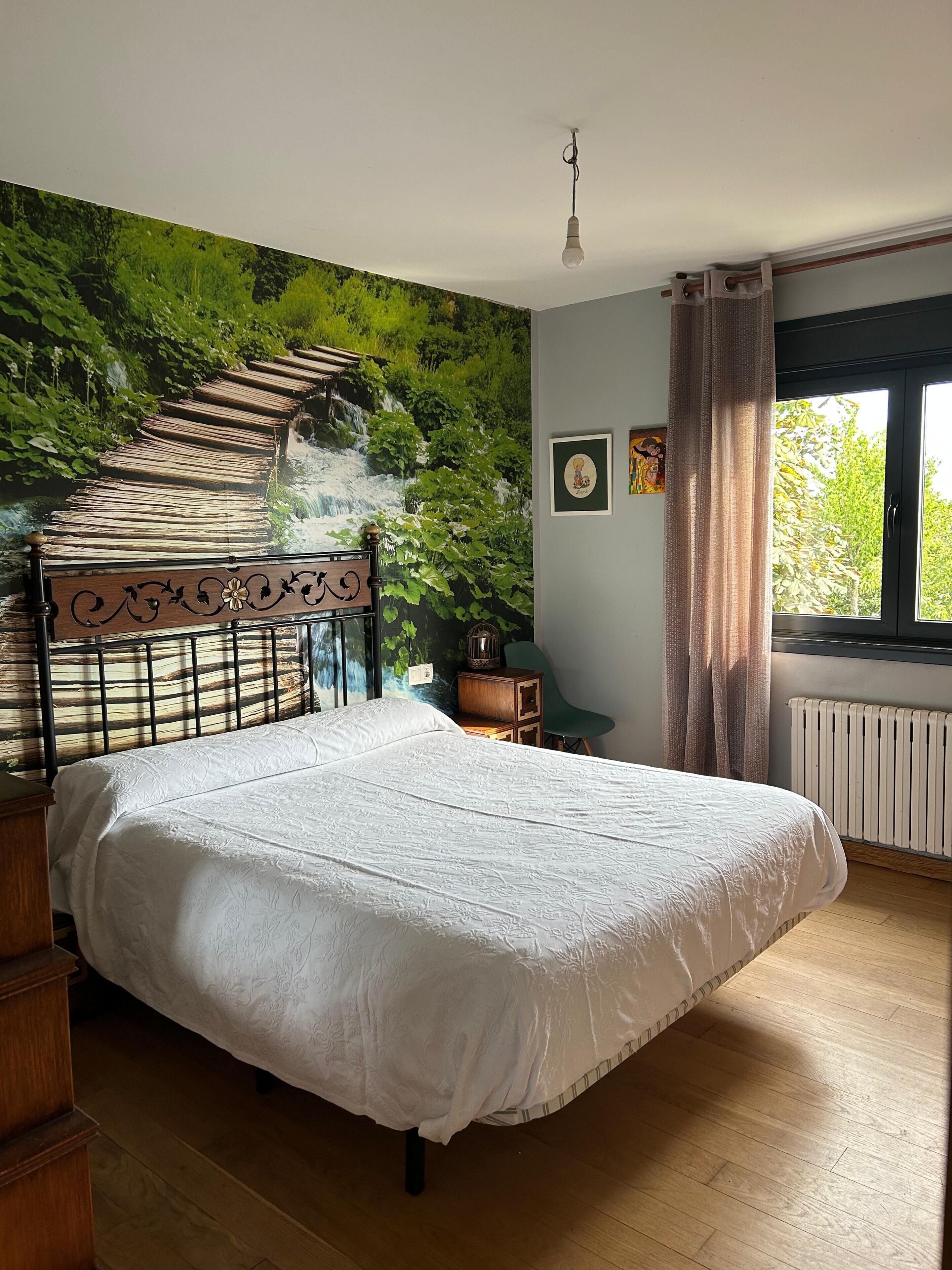 Ein Schlafzimmer mit einem Bett, Wandbild, Fenster und Heizkörper.