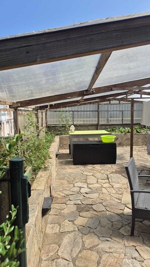 A covered outdoor area with a stone floor, a table, and a bench.