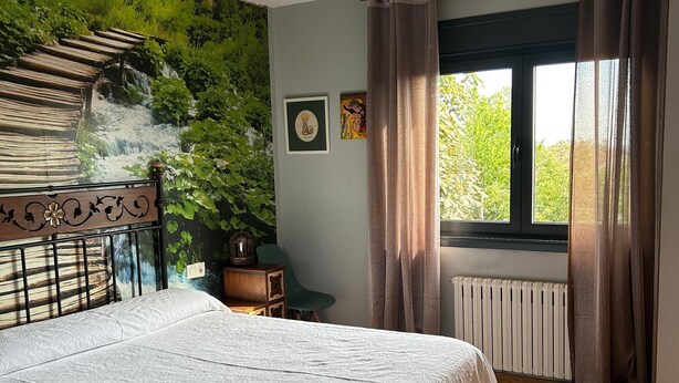A bedroom with a bed, a radiator, a window with curtains, and a wall mural.