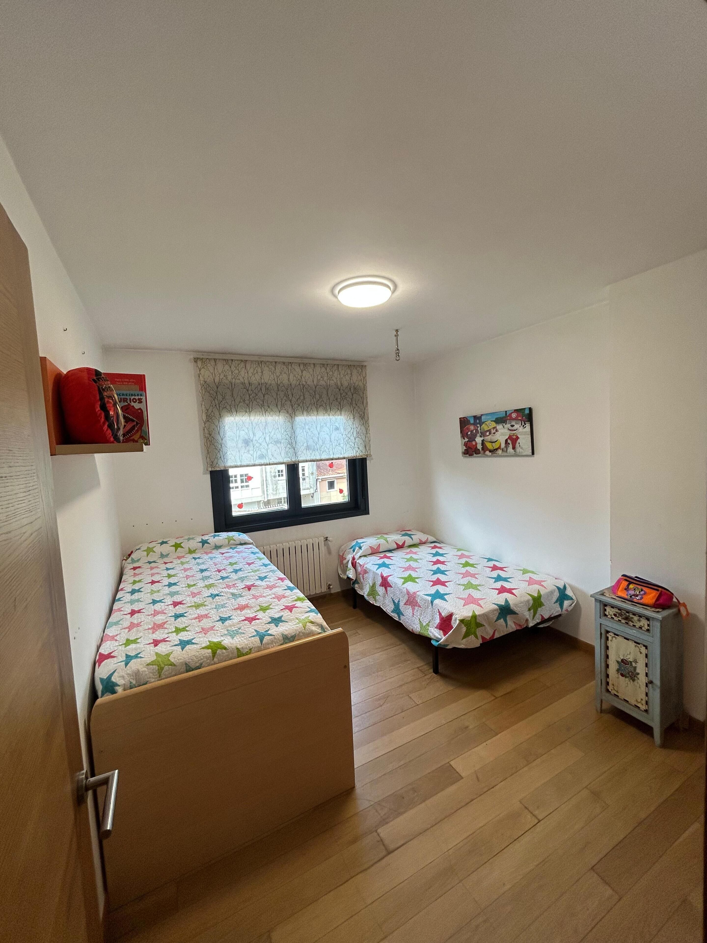 A room with two beds, a radiator, a window with a view, a door, and a small cabinet.