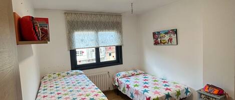 A room with two beds, a radiator, a window with a view, a door, and a small cabinet.