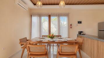 Comedor con mesa de madera dispuesta para cuatro personas, rodeada de sillas de mimbre, bajo un techo de madera con lámparas colgantes.