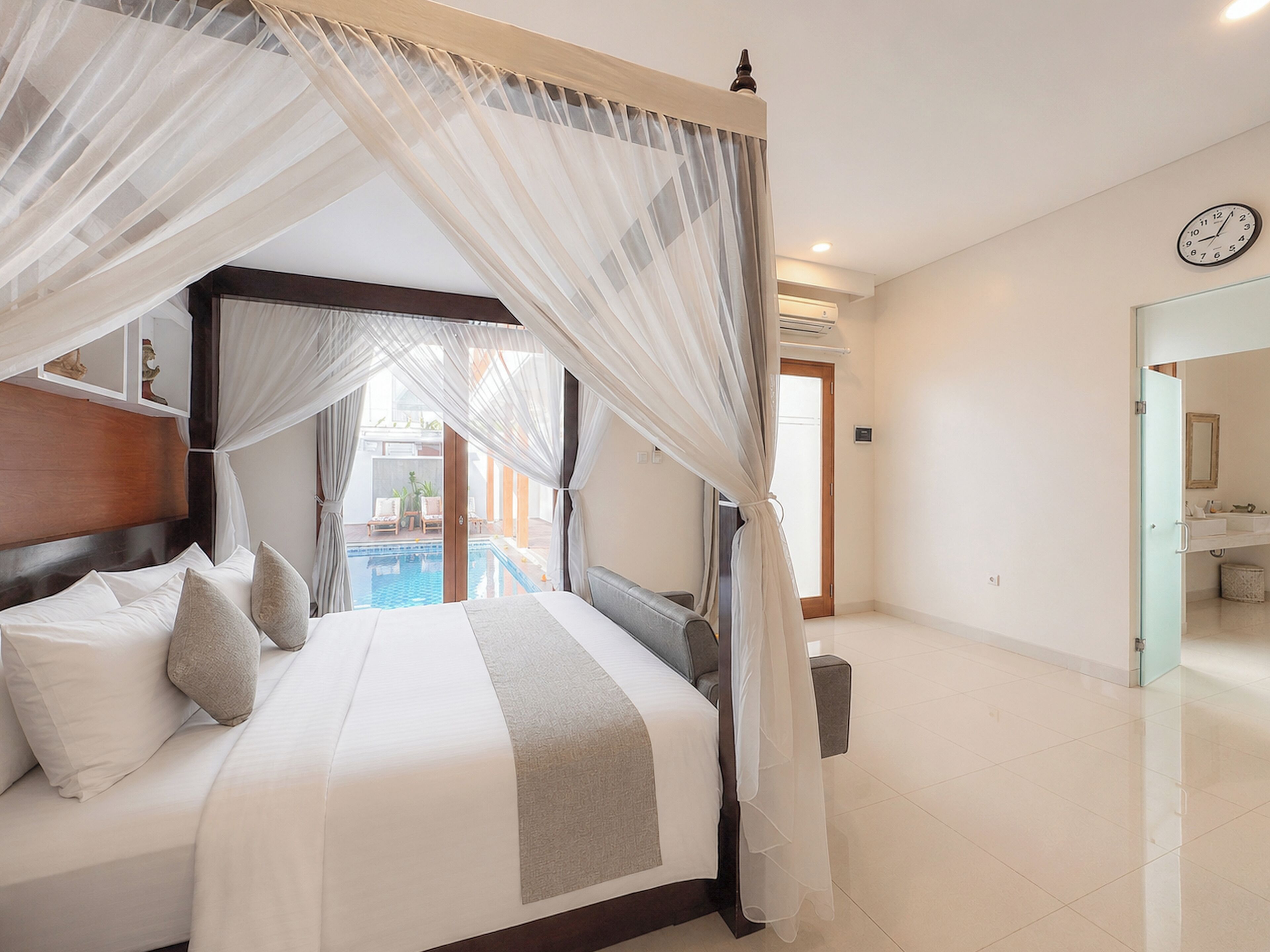 Quarto com cama de dossel, vista para uma piscina e banheiro com pia e espelho.
