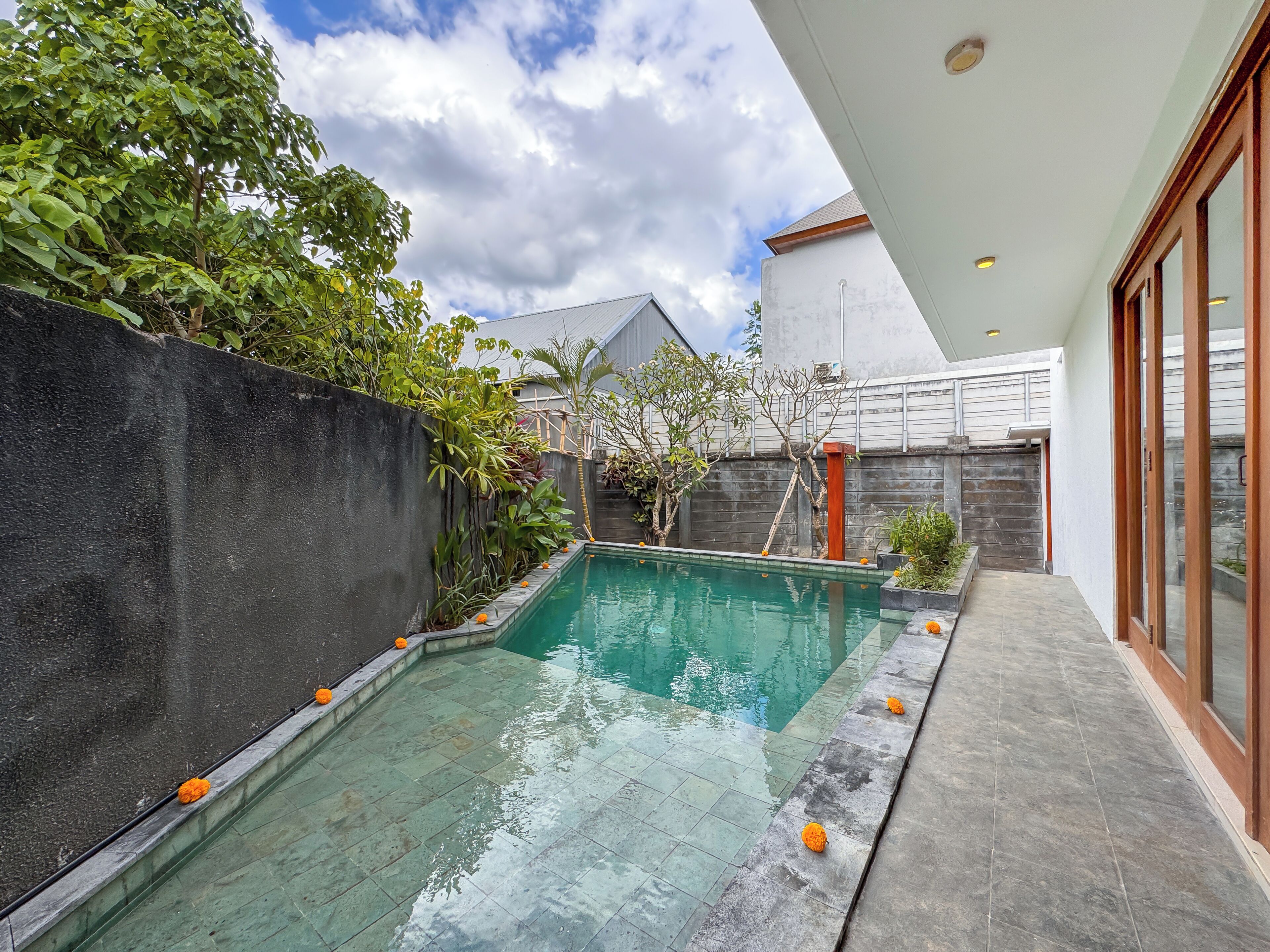 Una piscina con borde de baldosas, rodeada por un muro bajo y vegetación.