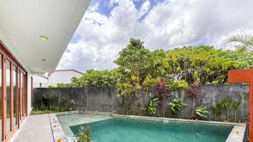 Piscina retangular com borda azulejada, rodeada por diversos tipos de plantas e um muro de concreto.