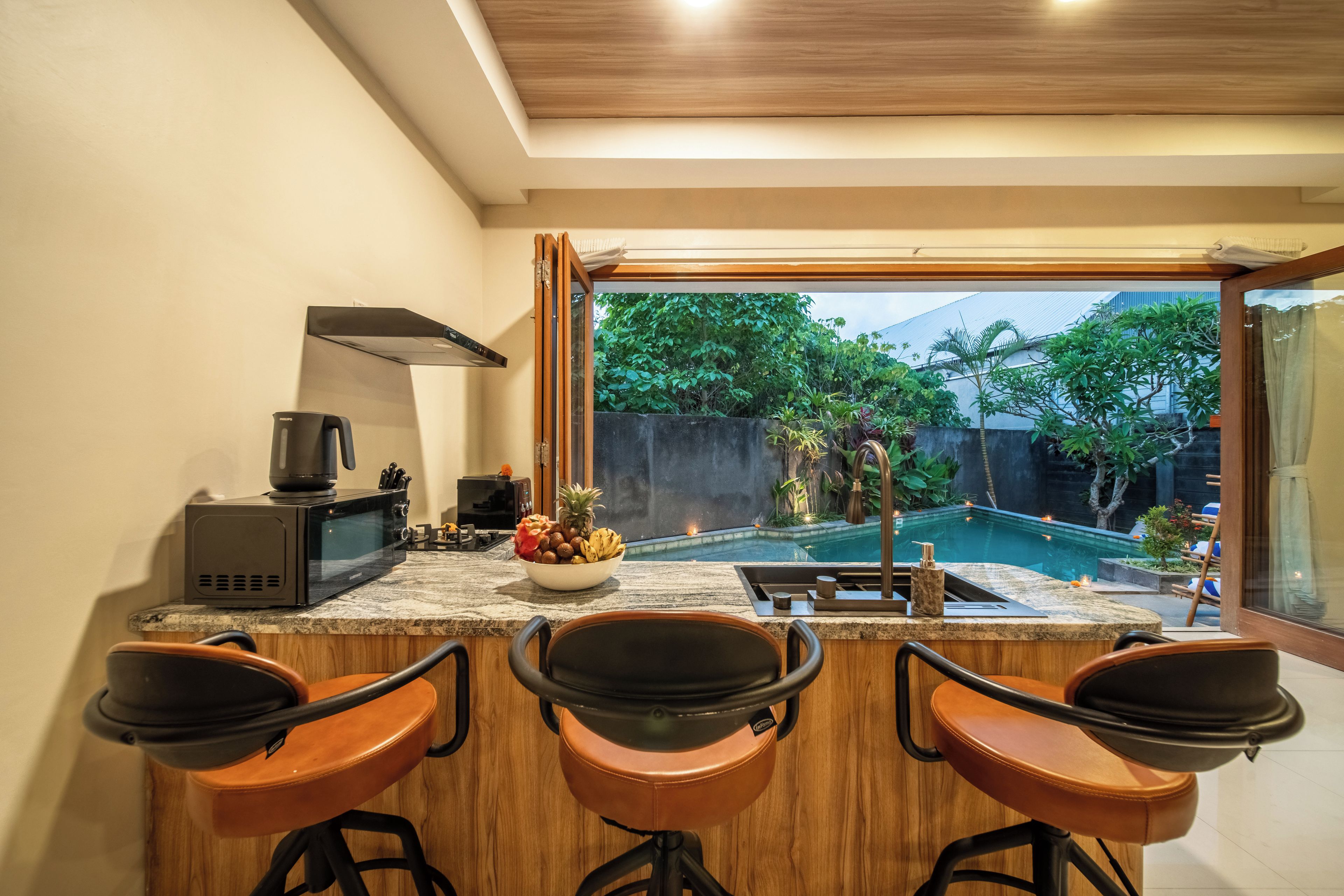 A kitchen with a large window, a microwave, a toaster, and a bowl of fruit.