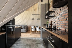 A modern kitchen with a brick wall, wooden ceiling, and a dining area with a sofa and chairs.